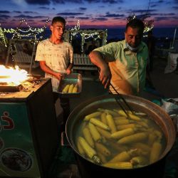 Hombres palestinos preparan mazorcas de maíz a la parrilla en su puesto al atardecer en la costa de la ciudad de Gaza. | Foto:Mohammed Abed / AFP
