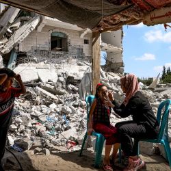 Una mujer palestina pinta una bandera nacional en la cara de un niño, entre los escombros de los edificios destruidos por el bombardeo israelí del mes pasado sobre la Franja de Gaza, en Beit Lahia, en el norte del enclave palestino. | Foto:Mahmud Hams / AFP