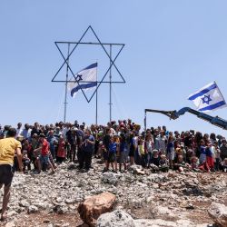 Colonos israelíes se reúnen para una fotografía de grupo bajo una estrella de David gigante y una bandera nacional antes de evacuar el puesto de avanzada de Eviatar recientemente establecido en Beita, cerca de la ciudad norteña palestina de Nablus en la Cisjordania ocupada. | Foto:Emmanuel Dunand / AFP