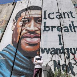 El artista palestino Taqi Spateen posa ante un mural de su creación que representa a George Floyd, un hombre negro desarmado que murió después de que un policía blanco se arrodillara sobre su cuello durante un arresto en Estados Unidos en mayo de 2020, pintado en una sección de la polémica barrera de separación de Israel en Belén. | Foto:Emmanuel Dunand / AFP