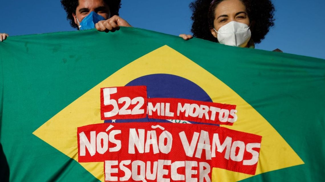 People holding a Brazilian flag that reads "522,000 deaths, we won't forget" take part in a demonstration against the Brazilian President Jair Bolsonaro's handling of the COVID-19 pandemic in Brasilia, on July 3, 2021.