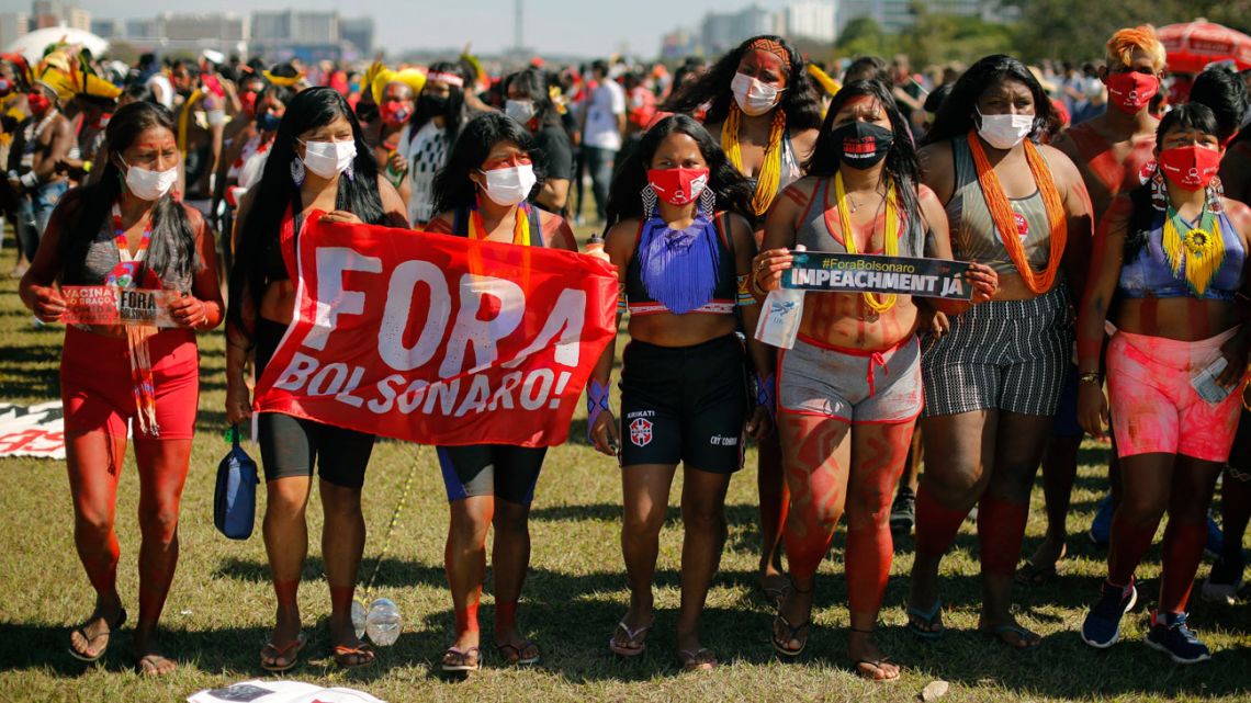 In this file photo taken on June 19, 2021, Brazilian indigenous women take part in a protest by opposition parties and social movements against Brazilian President Jair Bolsonaro's handling of the COVID-19 pandemic in Brasilia. The government of Jair Bolsonaro and his agribusiness allies in Congress accelerate the processing of projects seen by indigenous people as threats to their ancestral lands. 