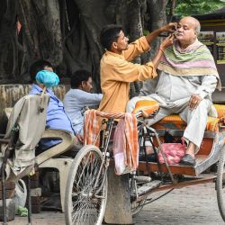 Un hombre se afeita la barba mientras se sienta en un rickshaw en una acera de Amritsar. | Foto:Narinder Nanu / AFP