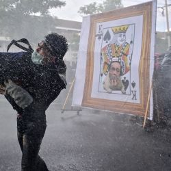 Un manifestante prodemocrático lanza un objeto mientras otros se ponen a cubierto del cañón de agua de la policía tras una imagen despectiva del primer ministro de Tailandia, Prayut-Chan-O-Cha, mientras marchan hacia la Casa de Gobierno para pedir su dimisión en Bangkok. | Foto:Lillian Suwanrumpha / AFP