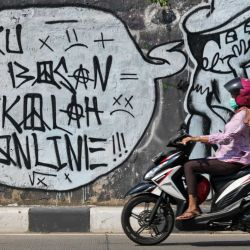 Una mujer pasa con su moto por delante de un mural en el que se lee  | Foto:Bay Ismoyo / AFP