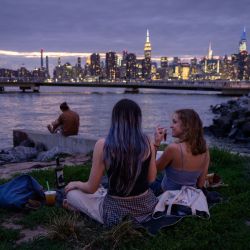 La gente se sienta ante el horizonte de la ciudad de Manhattan, en Brooklyn, Nueva York. | Foto:Ed Jones / AFP