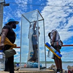 Migrantes varados de Haití, Cuba, Venezuela y varios países africanos pasan por delante de una estatua de la Virgen en un muelle antes de subir a un barco hacia Capurganá, cerca de la frontera con Panamá, en Necoclí, Colombia. | Foto:Joaquin Sarmiento / AFP