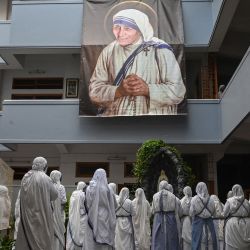 Monjas de las Misioneras de la Caridad asisten a una oración especial para conmemorar el 111º aniversario del nacimiento de la Madre Teresa, cerca de una pancarta con su imagen en la Casa de la Madre en Calcuta. | Foto:Dibyangshu Sarkar / AFP