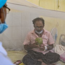 Un paciente bebe agua de coco mientras está sentado bajo un mosquitero en una sala de dengue de un hospital gubernamental en Allahabad. | Foto:Sanjay Kanojia / AFP