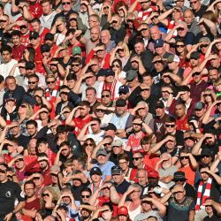 Árbitro asistente y aficionados del Liverpool se protegen los ojos contra el sol bajo durante el partido de fútbol de la Premier League inglesa entre el Liverpool y el Chelsea en Anfield, en Liverpool, noroeste de Inglaterra. | Foto:Paul Ellis / AFP
