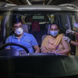 Un trabajador sanitario inocula a una mujer sentada en el interior de un coche con la vacuna Covishield contra el coronavirus Covid-19 durante un campamento de vacunación en coche instalado en el sótano de un centro comercial en Vashi. | Foto:Indranil Mukherjee / AFP