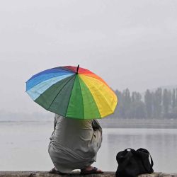 Un hombre sostiene un paraguas durante una lluvia mientras pesca en las orillas del lago Dal en Srinagar. | Foto:AFP