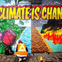 Artistas callejeros pintan un mural en una pared frente a la sede de la cumbre del clima COP26 en Glasgow. | Foto:Andy Buchanan / AFP