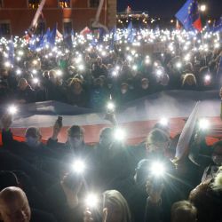 Los participantes muestran la luz de sus teléfonos móviles y ondean banderas de la UE sobre una gran bandera polaca mientras participan en una manifestación a favor de la UE tras una sentencia del Tribunal Constitucional contra la primacía del derecho de la UE en Polonia, frente al Castillo Real en la plaza central de Varsovia. | Foto:Wojtek Radwanski / AFP