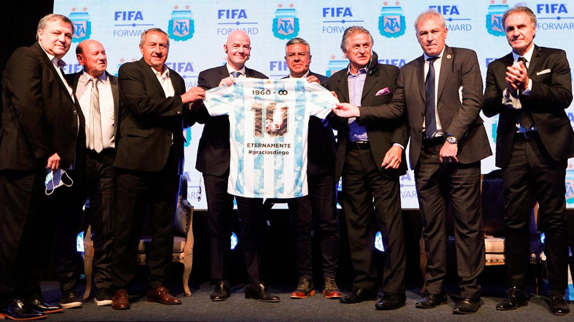 Handout photo released by Argentine Football Association (AFA) shows FIFA's President Gianni Infantino receiving a jersey from AFA chief Claudio Tapia and former players from Argentina's Mexico 1986 World Cup-winning team at AFA's training camp in Ezezia, Buenos Aires Province, on October 18, 2021. 