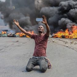 Un hombre se filma delante de unos neumáticos en llamas durante la huelga general lanzada por varias asociaciones profesionales y empresas para denunciar la inseguridad en Puerto Príncipe. | Foto:RICHARD PIERRIN / AFP