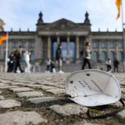 Una máscara protectora se ve en el suelo mientras los transeúntes caminan frente al edificio del Reichstag que alberga la cámara baja del parlamento Bundestag en Berlín, Alemania. | Foto:INA FASSBENDER / AFP