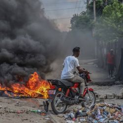 Un hombre conduce su bicicleta alrededor de unos neumáticos en llamas encendidos tras la convocatoria de una huelga general por parte de varias asociaciones profesionales y empresas para denunciar la inseguridad en Puerto Príncipe. | Foto:RICHARD PIERRIN / AFP