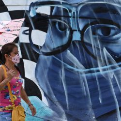 Una mujer pasa junto a un mural que representa a trabajadores sanitarios de primera línea con máscaras, a lo largo de una calle de Manila, Filipinas. | Foto:TED ALJIBE / AFP