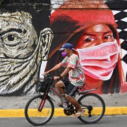 Un residente pasa en bicicleta junto a un mural que representa a trabajadores sanitarios de primera línea con máscaras, a lo largo de una calle de Manila. | Foto:TED ALJIBE / AFP