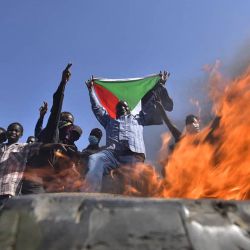 Un hombre sostiene una bandera nacional sudanesa ante las llamas de una barricada mientras la gente protesta contra el golpe militar en Sudán, en la "Calle 60" en el este de la capital Jartum. | Foto:AFP