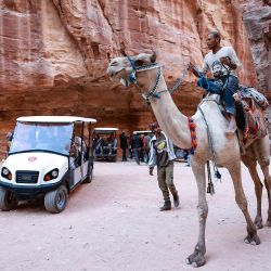 En la foto se ven turistas montados en camellos y otros en un carro eléctrico, durante su viaje a la famosa y antigua ciudad jordana de Petra, a unos 230 km al sur de la capital, Ammán. | Foto:KHALIL MAZRAAWI / AFP