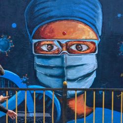 Un hombre pasa por delante de un mural que representa a un trabajador sanitario para concienciar sobre el coronavirus Covid-19 en Mumbai. | Foto:PUNIT PARANJPE / AFP