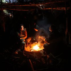 Un grupo de migrantes descansa junto a una hoguera en un campamento cerca de la frontera bielorrusa-polaca en la región de Grodno. | Foto:LEONID SHCHEGLOV / BELTA / AFP