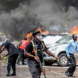 Unas personas apagan el fuego de los coches causado por la explosión de una bomba cerca del edificio del Parlamento en Kampala, Uganda. | Foto:Ivan Kabuye / AFP