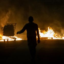 Una persona camina cerca de una barricada en llamas en una carretera de Le Lamentin, en la isla caribeña francesa de Martinica, tras más de una semana de violentas protestas provocadas por las restricciones del Covid-19. | Foto:ALAIN JOCARD / AFP