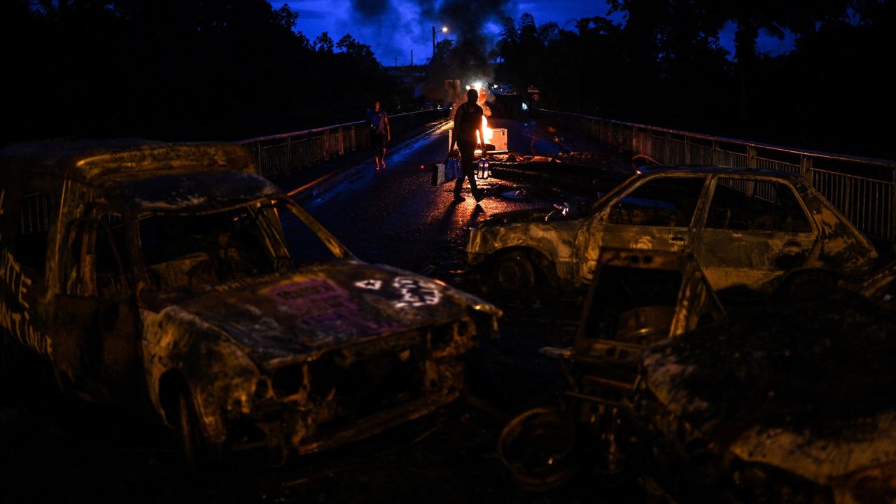 Un hombre lleva botellas de agua a través de un bloqueo de carretera en llamas hecho de vehículos quemados y escombros en Sainte-Rose, en la isla caribeña francesa de Guadalupe. | Foto:CHRISTOPHE ARCHAMBAULT / AFP
