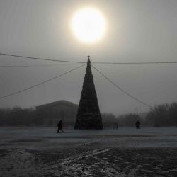 La gente pasa junto a un árbol de Navidad durante un día de niebla invernal en la ciudad de Baikonur, cerca del cosmódromo kazajo de Baikonur. Los turistas espaciales YusakuMaezawa y su asistente YozoHirano, liderados por el cosmonauta de Roscosmos Alexander Misurkin, participarán enuna misión en la nave espacial Soyuz MS-20 a la Estación Espacial Internacional (ISS) programada para el 8 de diciembre de 2021. | Foto:AFP