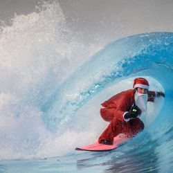 Un surfista vestido de Papá Noel monta una ola artificial en la piscina de olas de la bahía de Alaia, rodeada por los Alpes suizos, en Sion. | Foto:FABRICE COFFRINI / AFP
