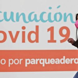 Una mujer pasa junto a un cartel que indica un punto de vacunación contra el COVID-19 en Bogotá, Colombia. | Foto:DANIEL MUNOZ / AFP
