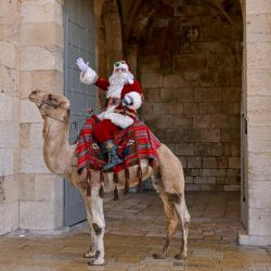 Un palestino vestido de Papá Noel gesticula mientras monta un camello en la Ciudad Vieja de Jerusalén durante las celebraciones navideñas. | Foto:AHMAD GHARABLI / AFP