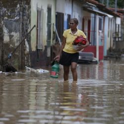Una mujer carga sus pertenencias mientras camina a través del agua de la inundación provocada por las fuertes lluvias, en Itapetinga, estado de Bahía, Brasil. | Foto:Xinhua/Lucio Tavora