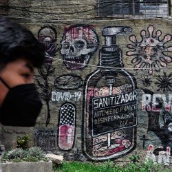  Un joven pasa junto a una pared con grafitis relacionados con el Covid-19 en La Paz, Bolivia. - Bolivia registra un récord nacional de más de 10.000 nuevos casos de Covid-19, y la mitad de las pruebas realizadas en el país han resultado positivas. | Foto:JORGE BERNAL / AFP
