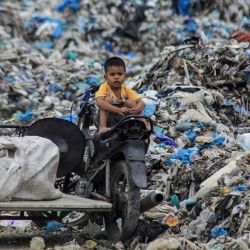Un niño se sienta en una bicicleta junto a la basura en el vertedero de Alue Lim en Lhokseumawe, Aceh, Indonesia. | Foto:AZWAR IPANK / AFP