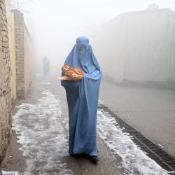 Una mujer con burka camina por una carretera en dirección a su casa después de recibir pan gratuito distribuido como parte de la campaña "Salvar a los afganos del hambre" en Kabul, Afganistan. | Foto:WAKIL KOHSAR / AFP