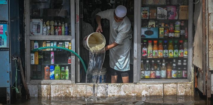 Un comerciante vierte el agua acumulada dentro de su tienda a lo largo de una calle anegada en una zona residencial después de una fuerte lluvia monzónica en Chennai, India.