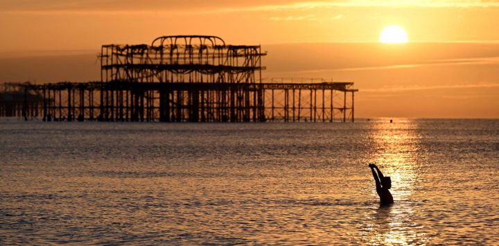Un nadador madrugador disfruta de su baño mientras el sol sale cerca del muelle oeste en Brighton, al sur de Inglaterra.