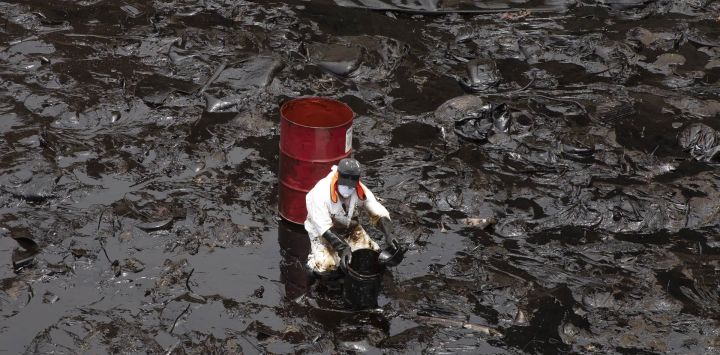 Un trabajador limpia el derrame de petróleo que se registró durante el proceso de descarga de crudo del buque Mare Dorium luego de un fuerte oleaje, en la playa de Ventanilla, en Callao, Perú.