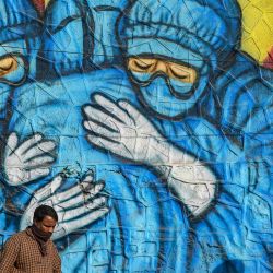 Peatones pasan por delante de un mural que representa a trabajadores sanitarios con trajes de equipo de protección personal para concienciar sobre el coronavirus Covid-19 en Mumbai, India. | Foto:PUNIT PARANJPE / AFP
