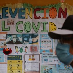 Una persona pasa junto a un cartel que da instrucciones sobre cómo prevenir el COVID-19 en medio de la pandemia del COVID-19 mientras se reanudan las clases presenciales después de las vacaciones en la unidad educativa Antonio Díaz Villamil en La Paz, Bolivia. | Foto:LUIS GANDARILLAS / AFP