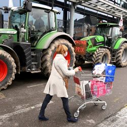 Un cliente pasa junto a los tractores de los miembros del sindicato de agricultores mientras llevan a cabo una operación destinada a controlar los precios y el origen de los productos en un supermercado de Rennes, al oeste de Francia. | Foto:DAMIEN MEYER / AFP