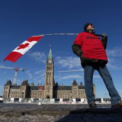 Un hombre sostiene una bandera canadiense cerca de la Colina del Parlamento mientras los manifestantes continúan protestando contra los mandatos de vacunación implementados por el primer ministro Justin Trudeau en Ottawa, Canadá. | Foto:Dave Chan / AFP