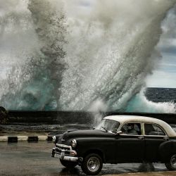 Un viejo coche americano circula mientras el fuerte viento empuja una ola en el malecón de La Habana, Cuba. | Foto:YAMIL LAGE / AFP