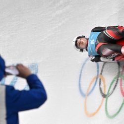 La canadiense Natalie Corless participa en el entrenamiento individual femenino de luge, pasando por delante de un espectador que capta la carrera con un smartphone, en el Centro Nacional de Deslizamiento de Yanqing durante los Juegos Olímpicos de Invierno de Pekín 2022. | Foto:DANIEL MIHAILESCU / AFP