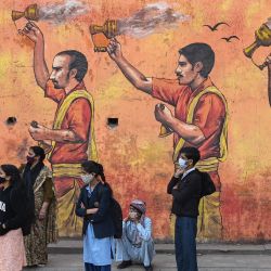 La gente espera un autobús en una carretera con el telón de fondo de un mural en Nueva Delhi, India. | Foto:Sajjad Hussain / AFP