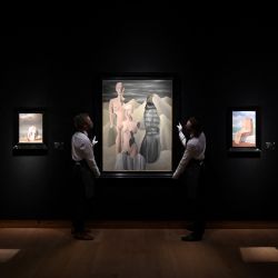 Asistentes de la galería sostienen una obra de arte titulada "La lumière du pôle" (Luz polar) del artista belga René Magritte junto a otras de sus obras durante un photocall en la casa de subastas Christie's de Londres. | Foto:JUSTIN TALLIS / AFP